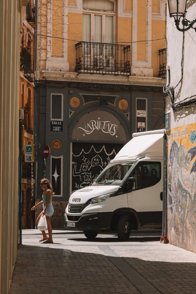 A woman walks near a white van on a vibrant European city street.